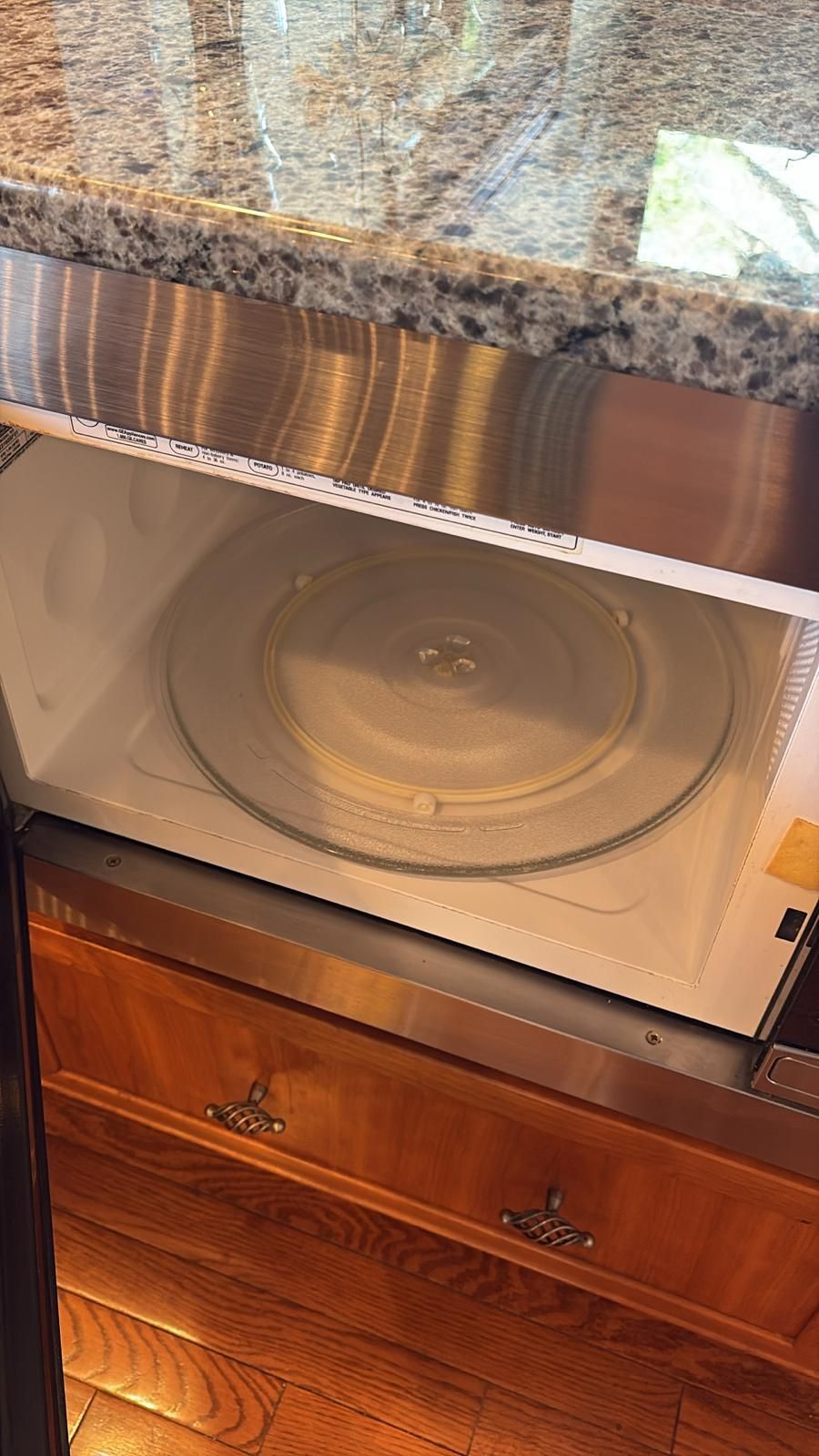 Open built-in microwave, showing glass turntable inside a stainless steel and wood cabinet.