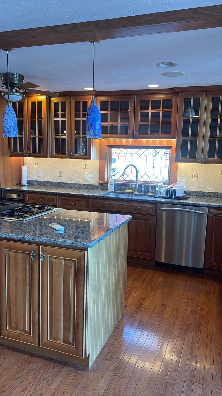 Kitchen with wooden cabinets, granite countertops, stainless steel appliances, and blue pendant lights.