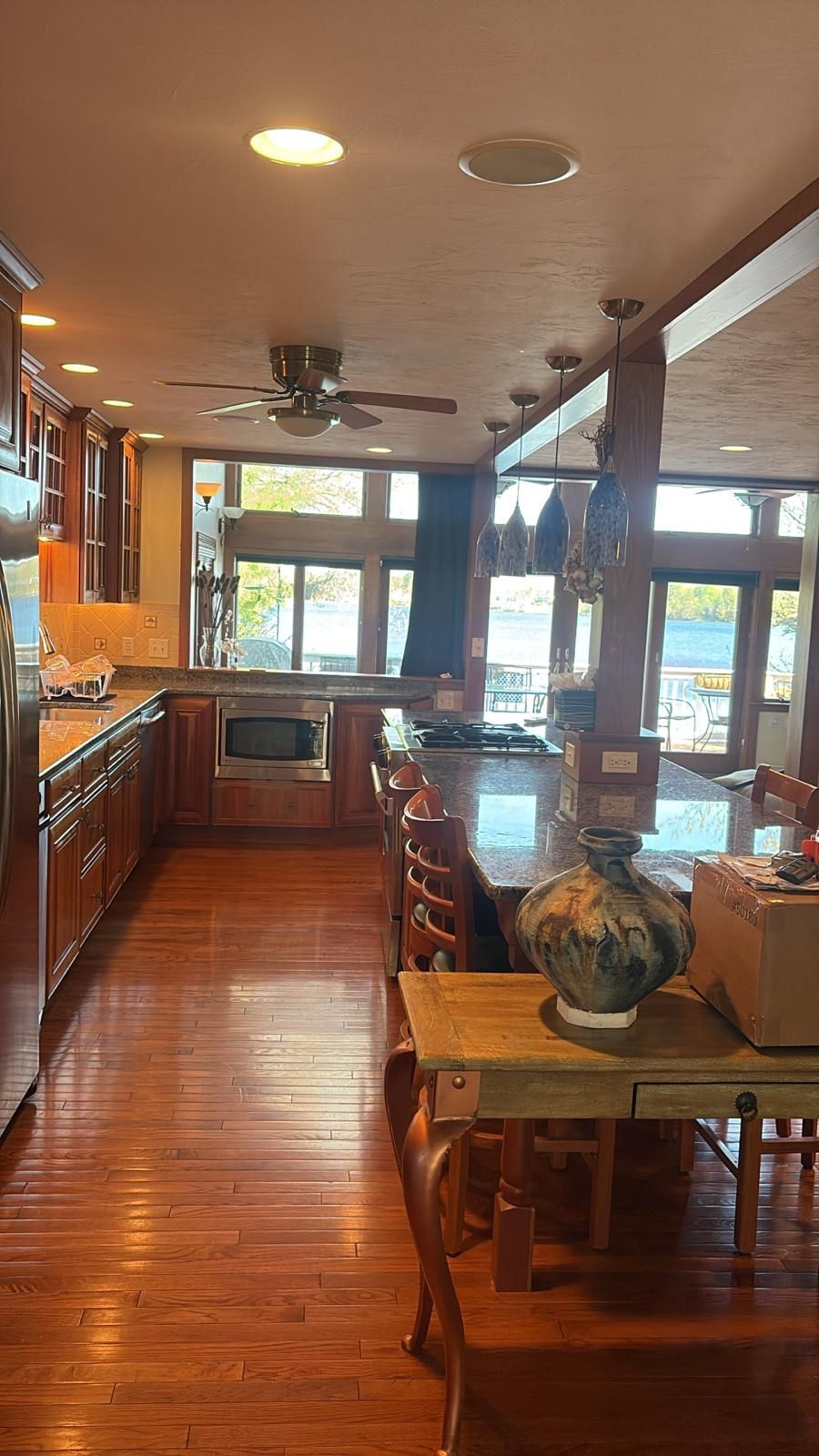 Kitchen with wooden cabinets, island, and dining table, with water visible through the windows.