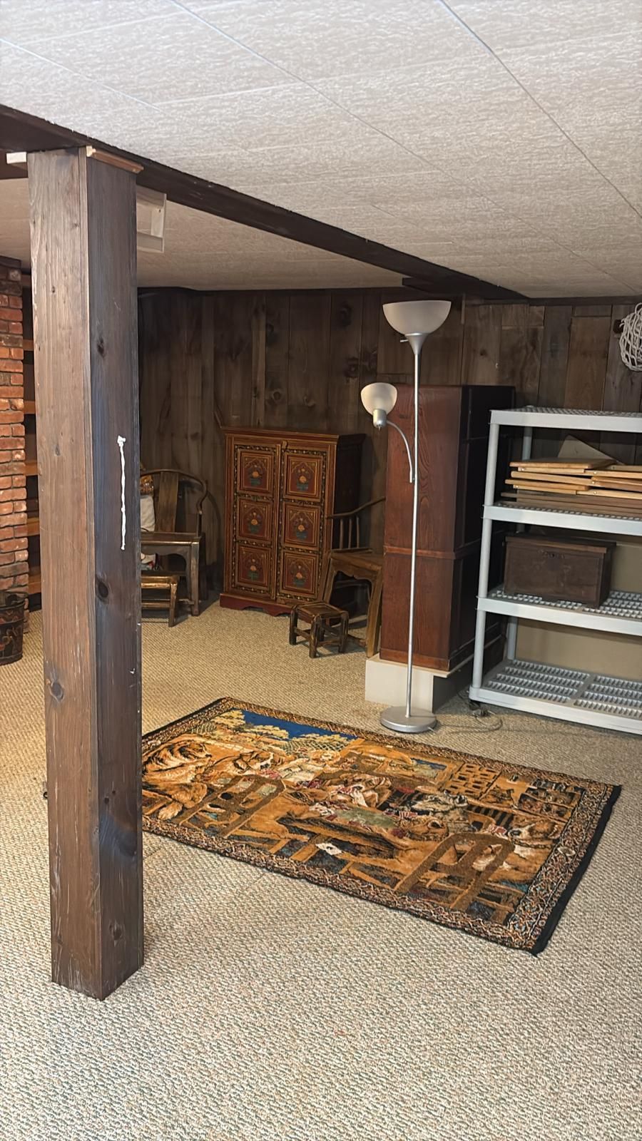 Basement with a rug, tall lamp, wooden beams, storage shelves, and a wooden pillar.