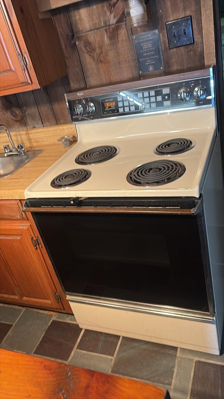 Cream-colored electric range with four burners, black oven door, in a kitchen with wood paneling.