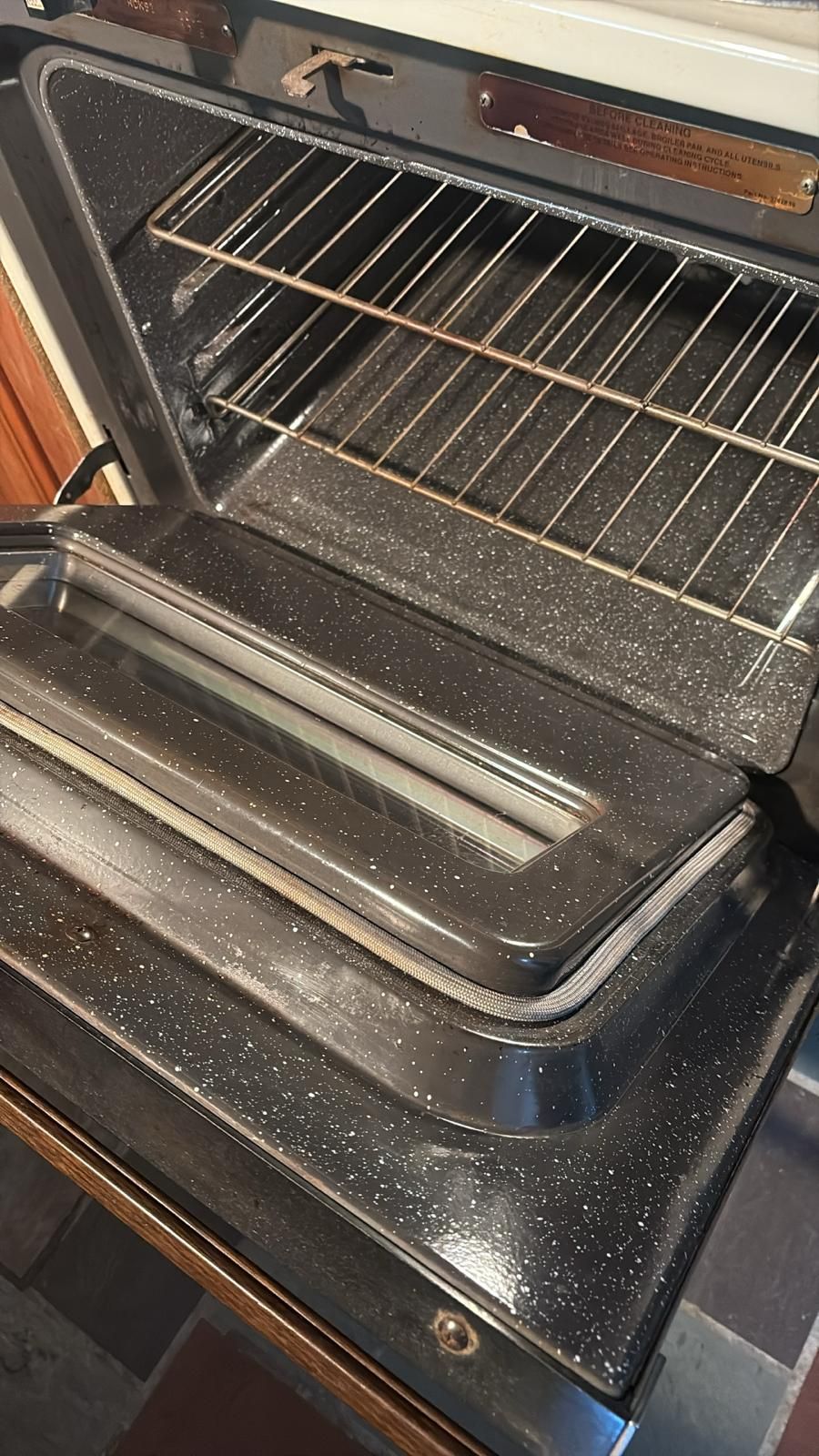 Open oven interior, with racks visible. Black speckled surfaces.