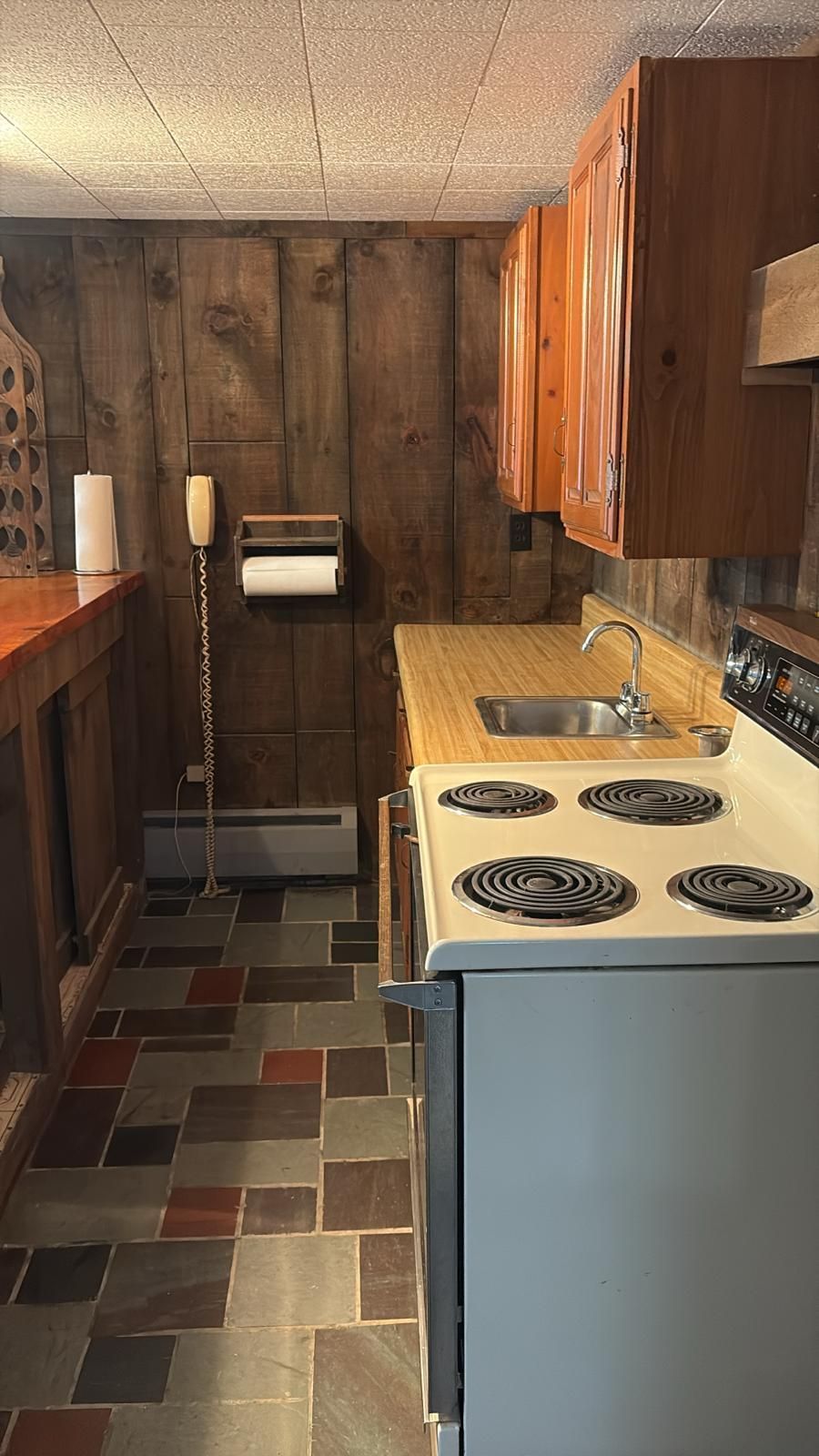 Small kitchen with wooden cabinets and paneling, a stove, and colorful tiled floor.