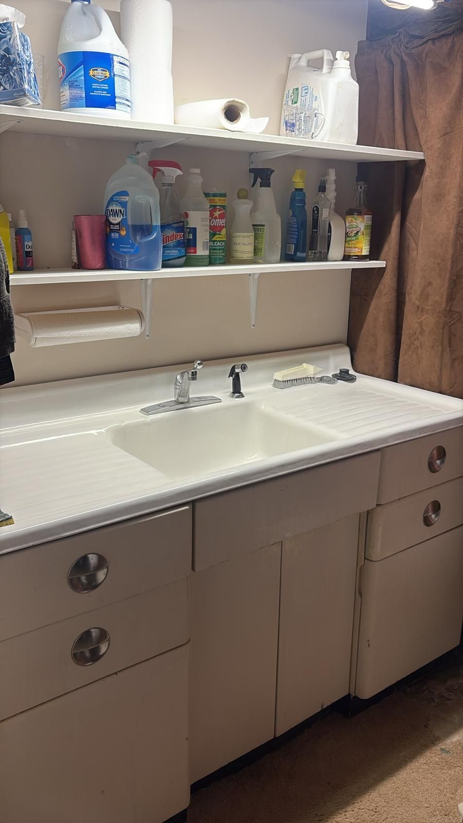 White utility sink with shelves above, holding cleaning supplies. Cabinets below.
