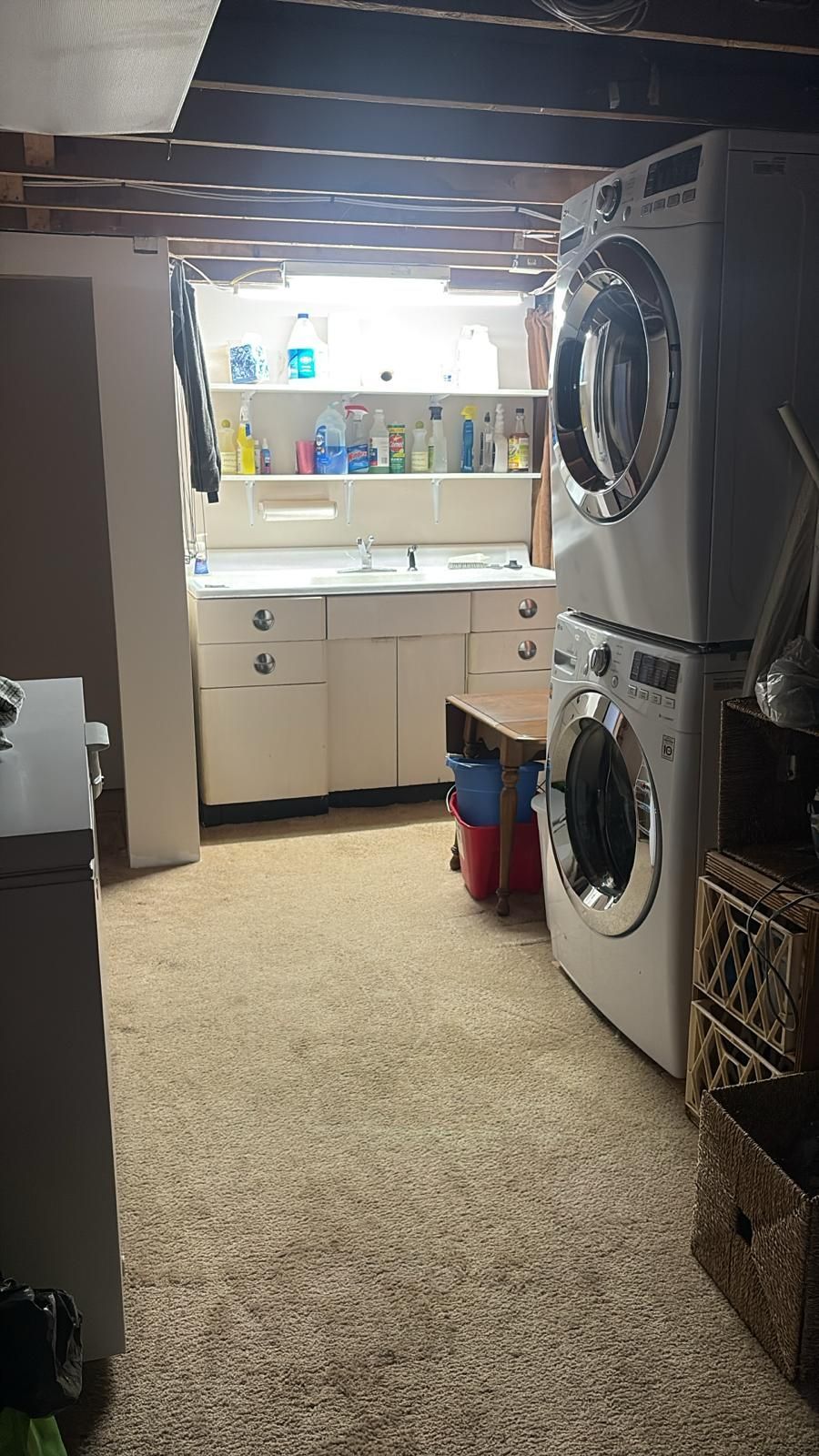 Laundry room with stacked white washer and dryer, sink, shelves with cleaning supplies.