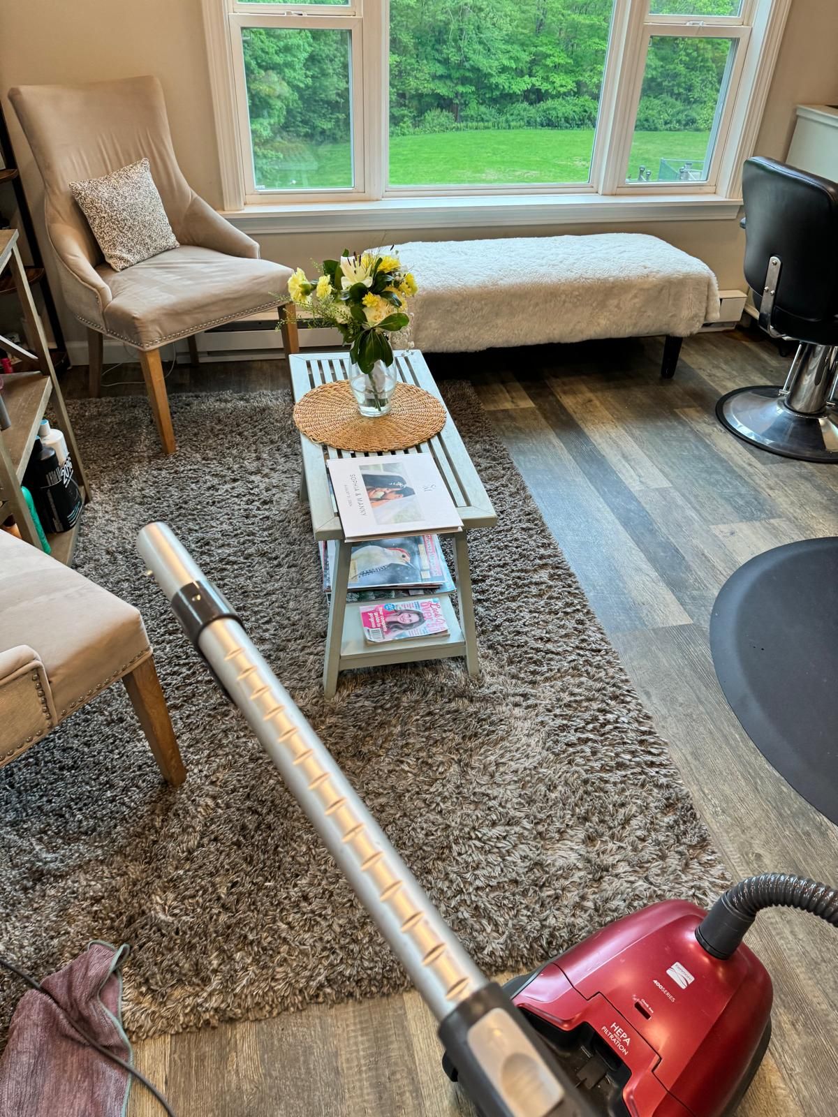 Vacuuming a gray shag rug in a waiting area with neutral chairs, a bench, and a window.