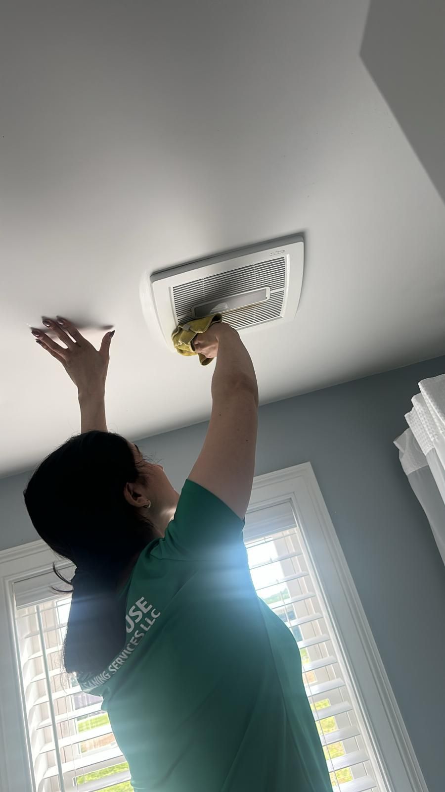 Woman cleaning a white ceiling vent with a yellow sponge.