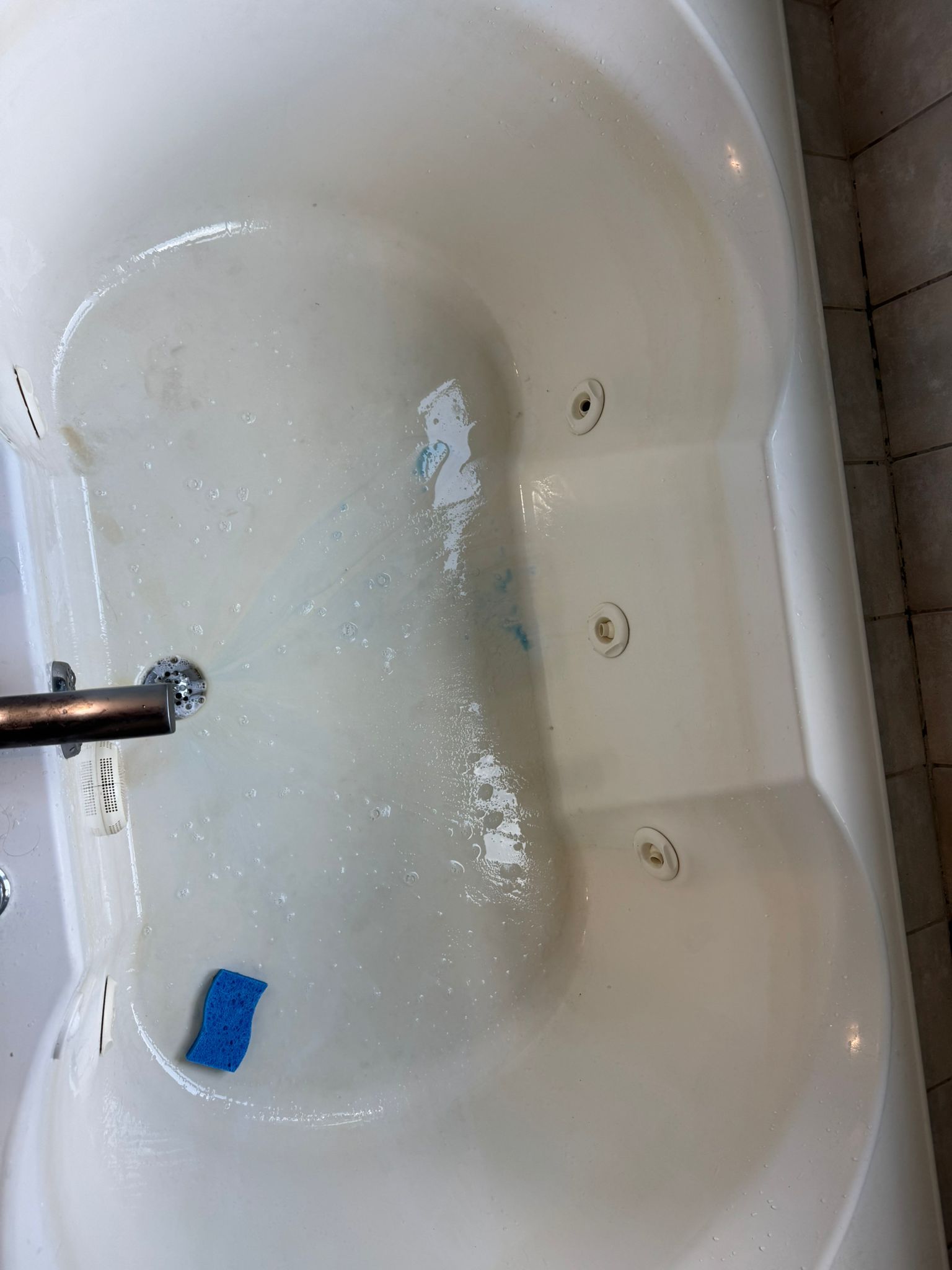White bathtub filled with water; various jets are visible on the sides of the tub.