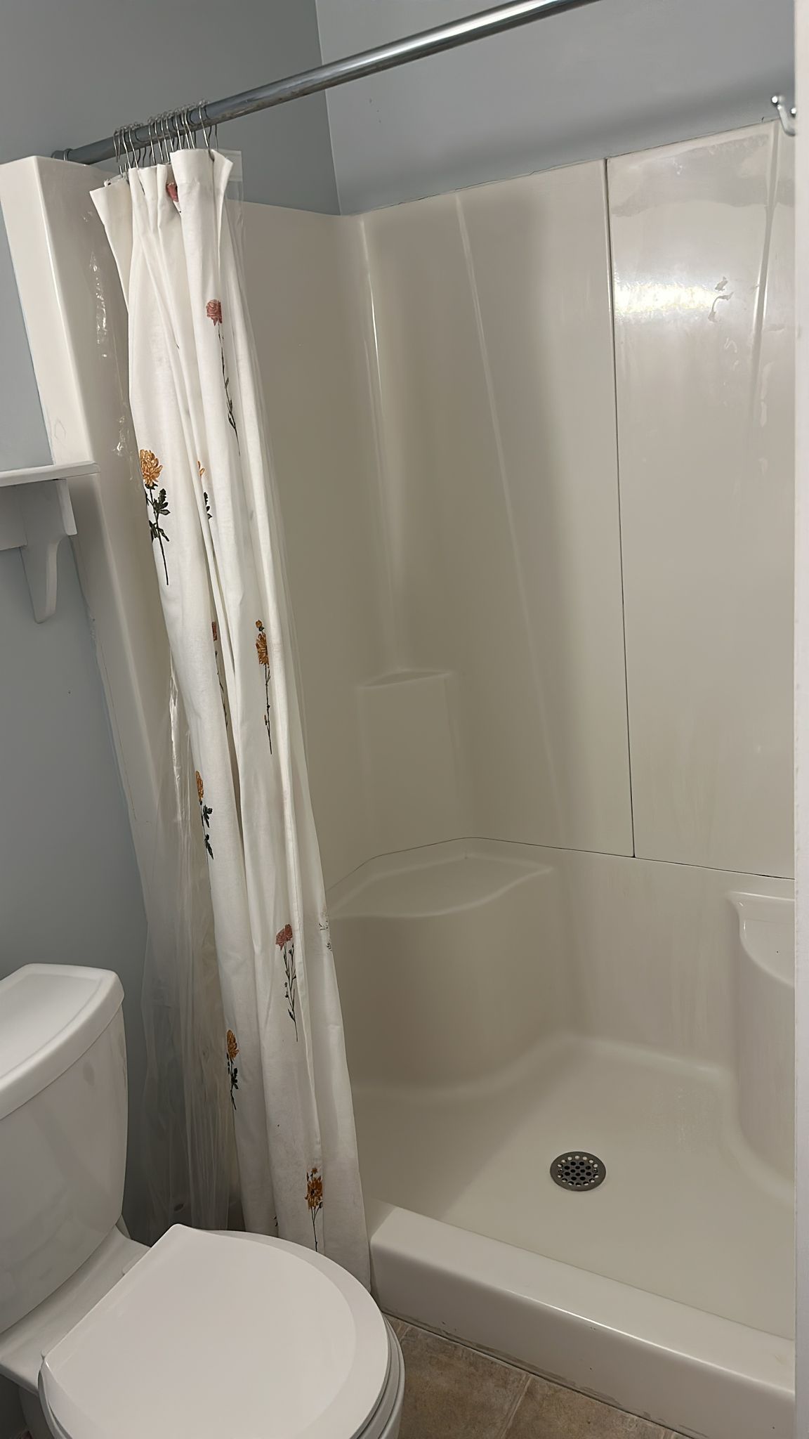 Bathroom with a white toilet, shower stall with a seat, and floral shower curtain.