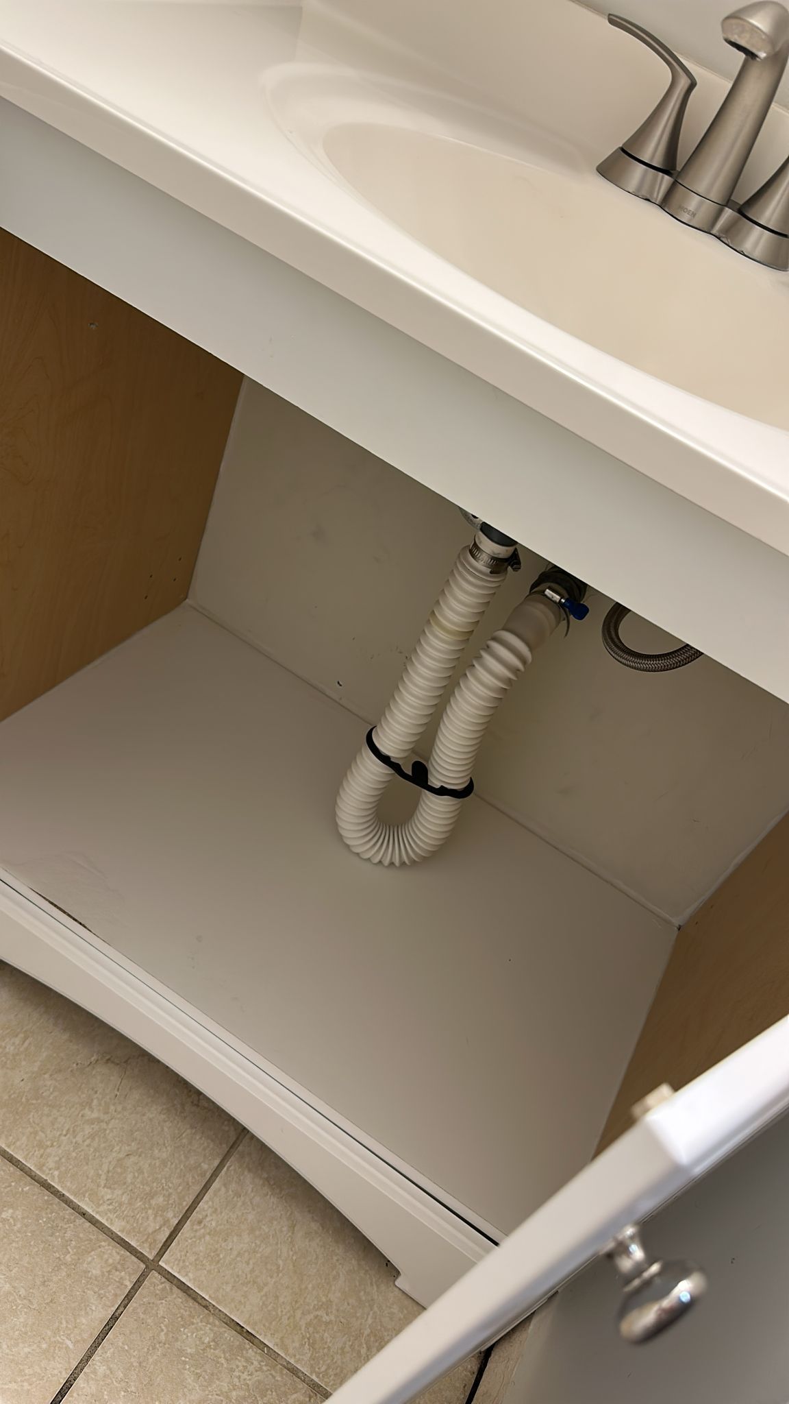 White bathroom sink cabinet interior with plumbing and sink basin visible.
