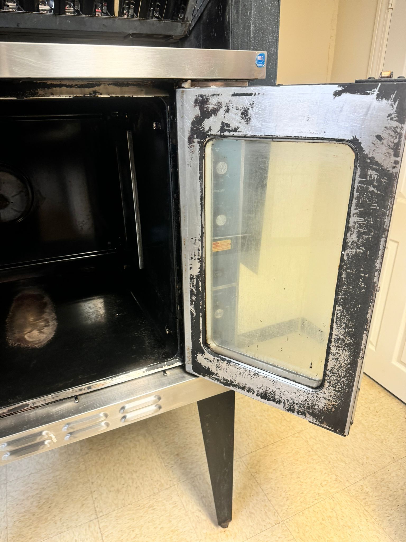 Open commercial oven with peeling black paint, showing the interior. Stainless steel trim.