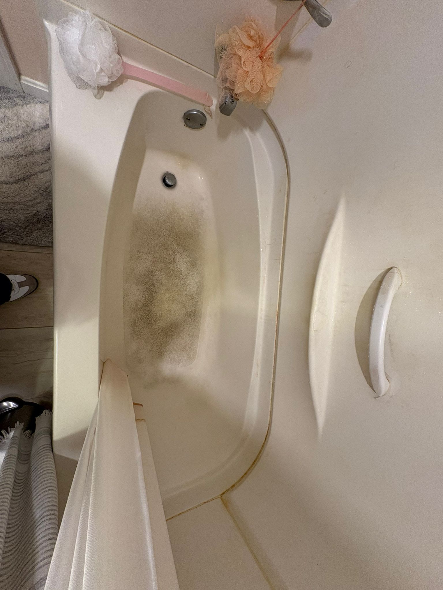 Dirty bathtub with dark mold stains. Soap and sponge hang nearby.