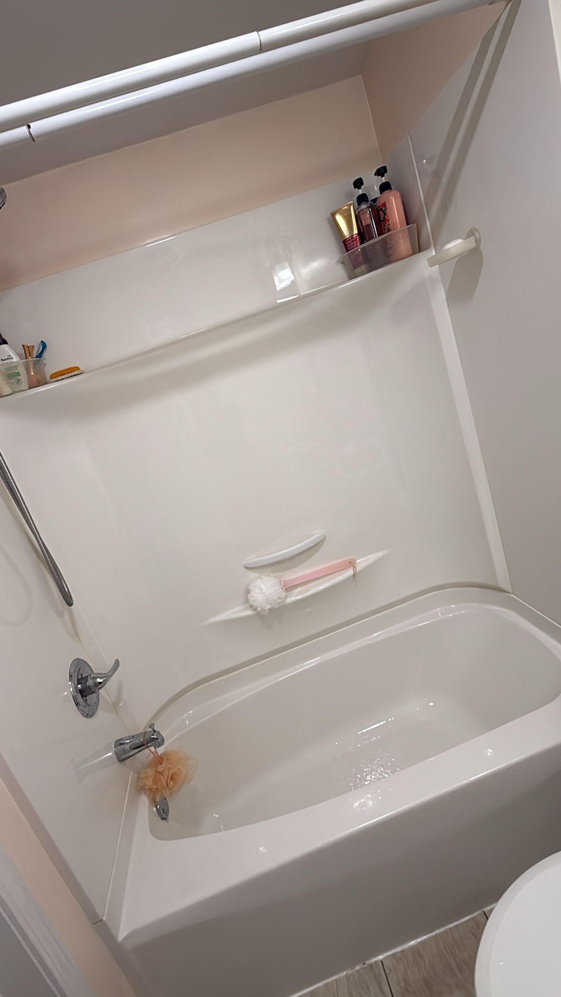 White bathtub in a shower enclosure with built-in shelves holding toiletries.