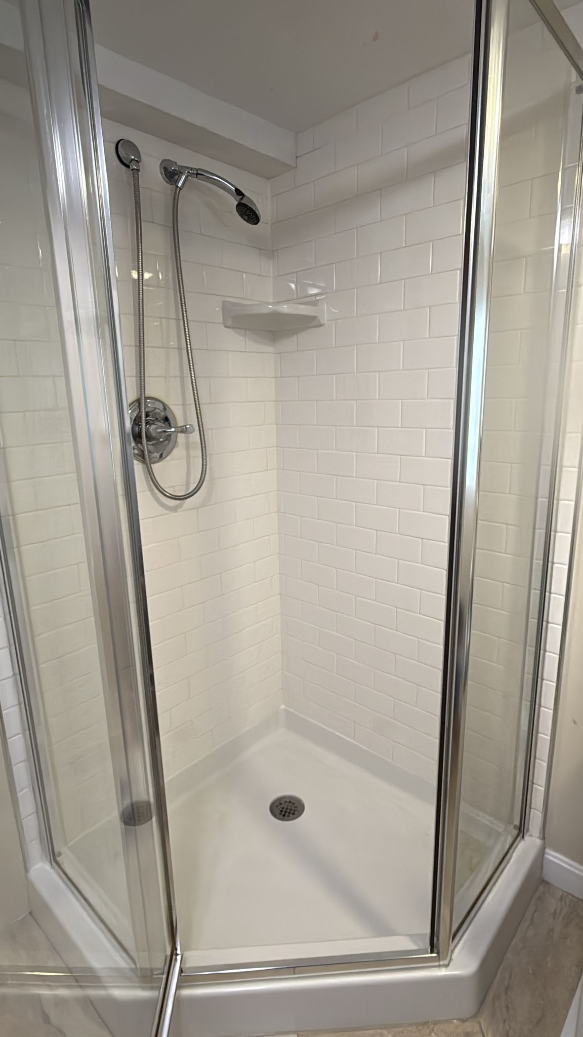 A clear glass shower with white tile walls, a built-in shelf, and chrome fixtures.
