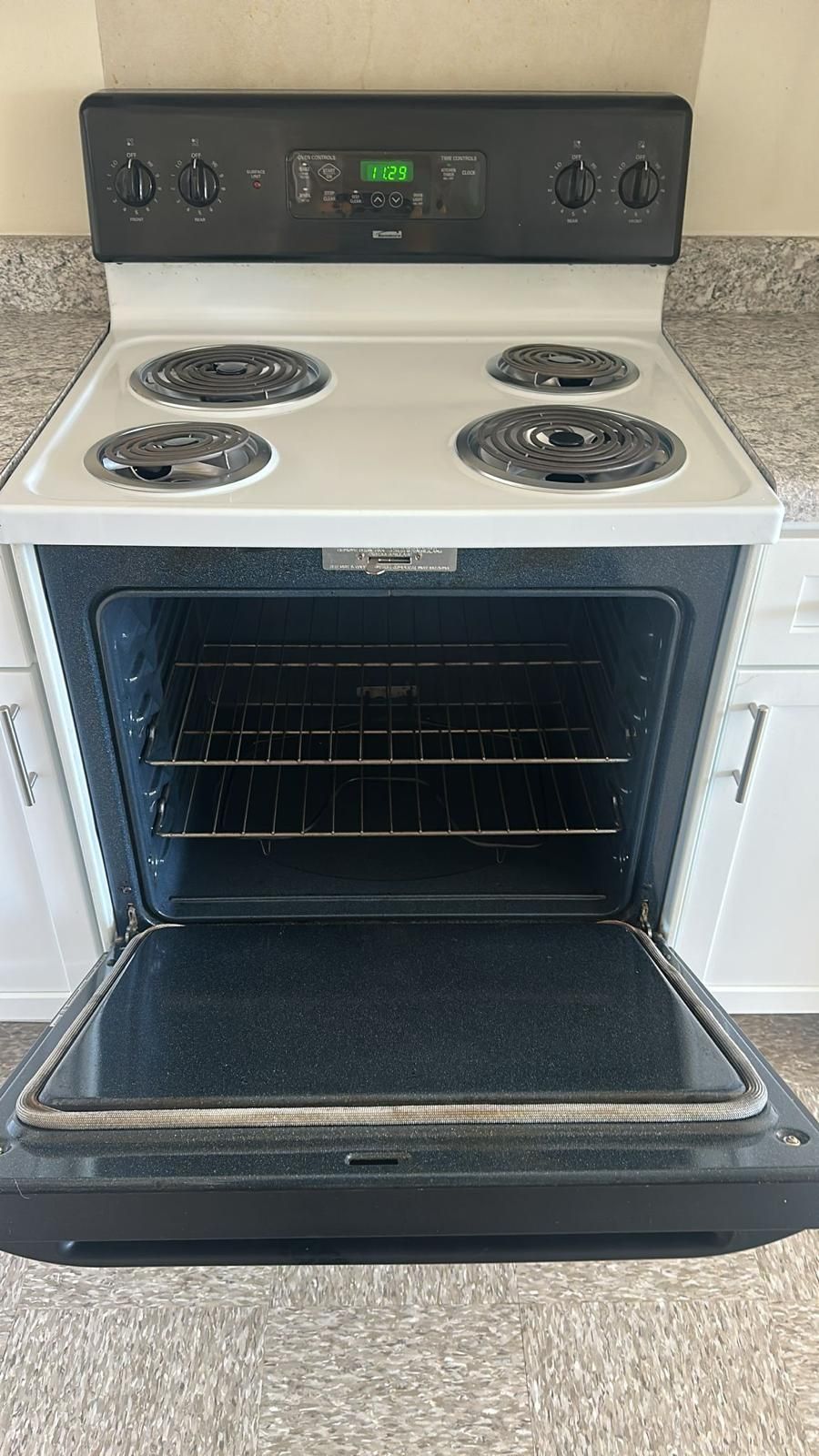 White electric Whirlpool oven with open door; black stovetop; empty oven interior.