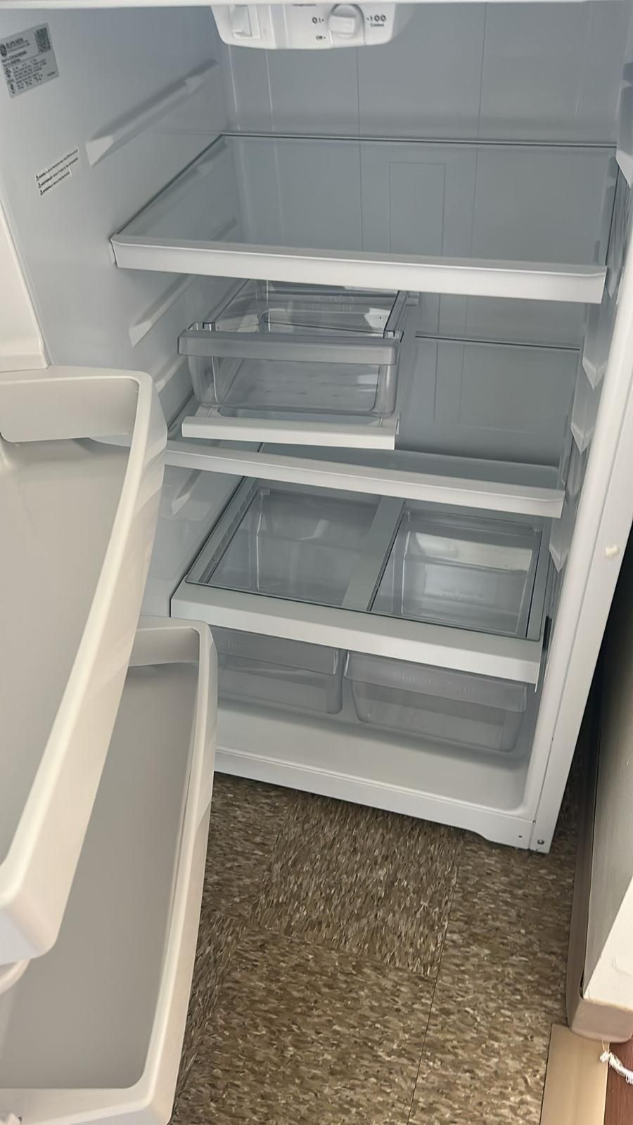 Open refrigerator interior; shelves, drawers, white, empty.