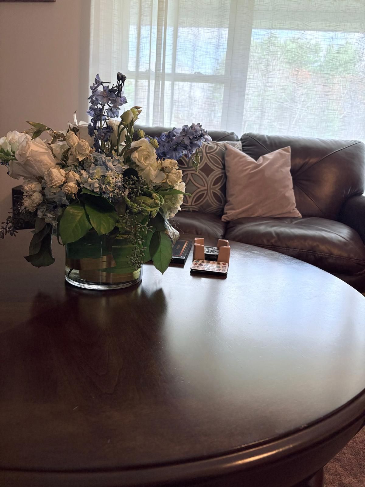 Round wooden table with a floral arrangement, remote, and couch in the background.