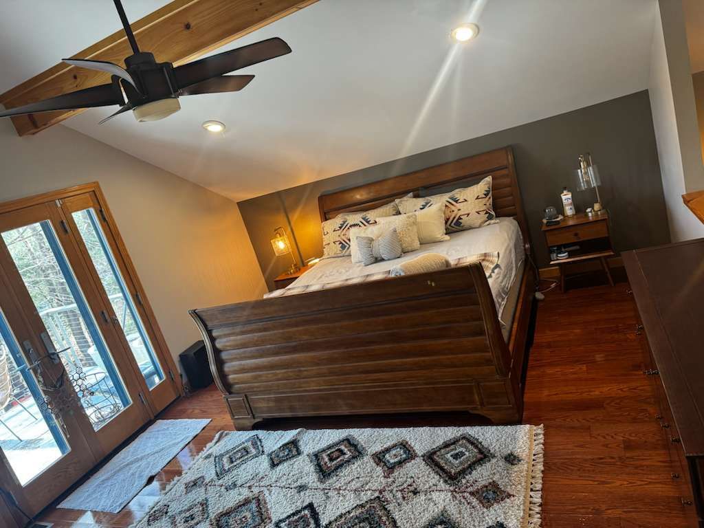 Bedroom with wooden bed, rug, and French doors; hardwood floor.