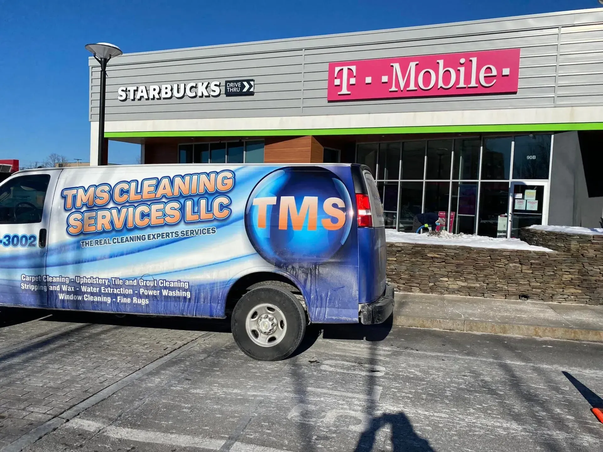 A TMS Cleaning Services van parked in front of a Starbucks and T-Mobile store.