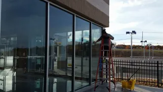 A person on a ladder washing windows of a building with large glass panes.