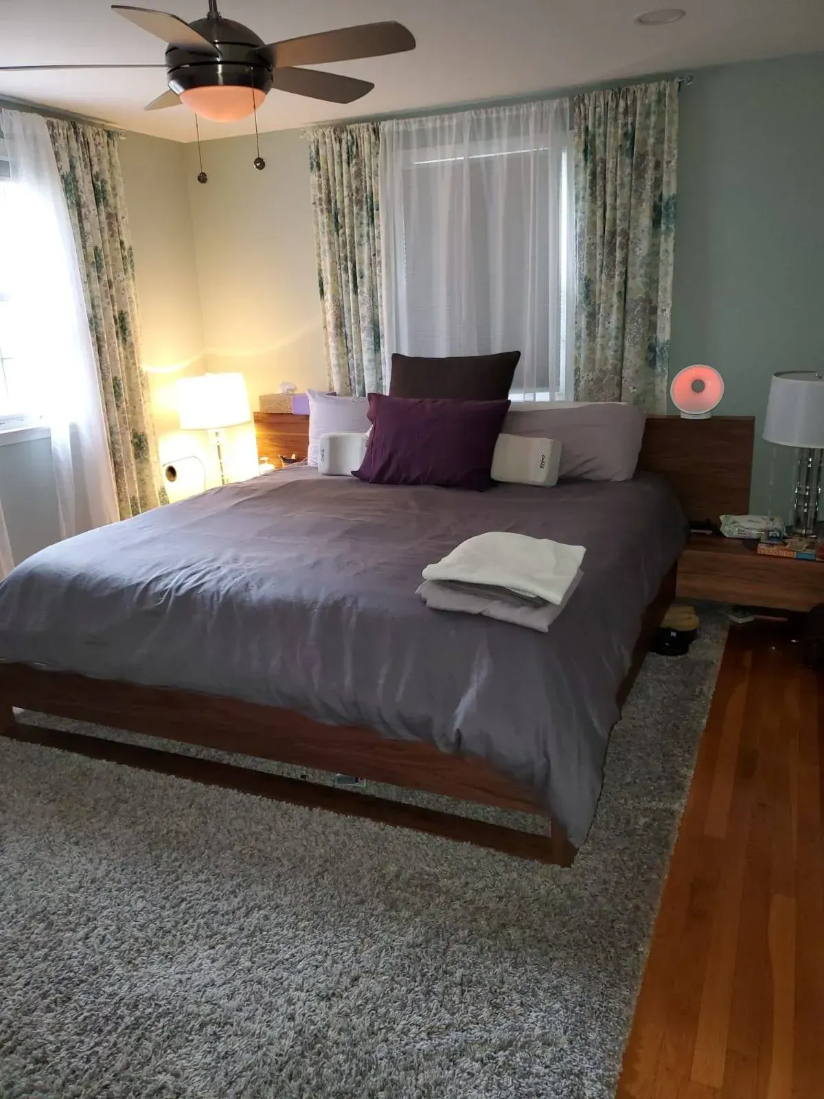 Bedroom with a gray bed, wood furniture, patterned curtains, and a fluffy gray carpet.