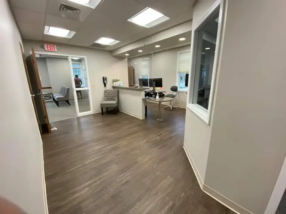 Interior view of a modern office reception area with a wooden floor, reception desk, and chairs.
