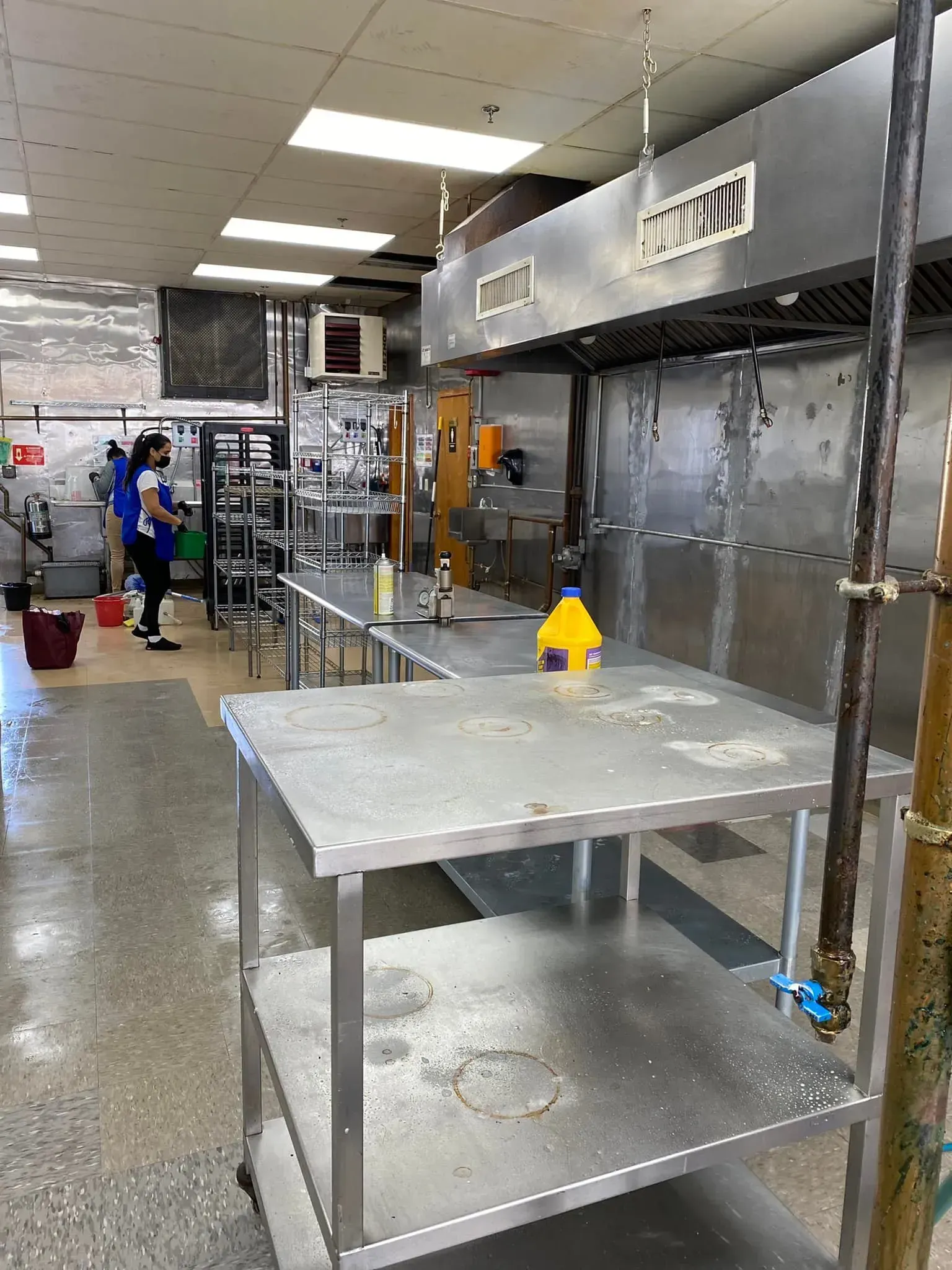Commercial kitchen with stainless steel tables, range hood, and a person.