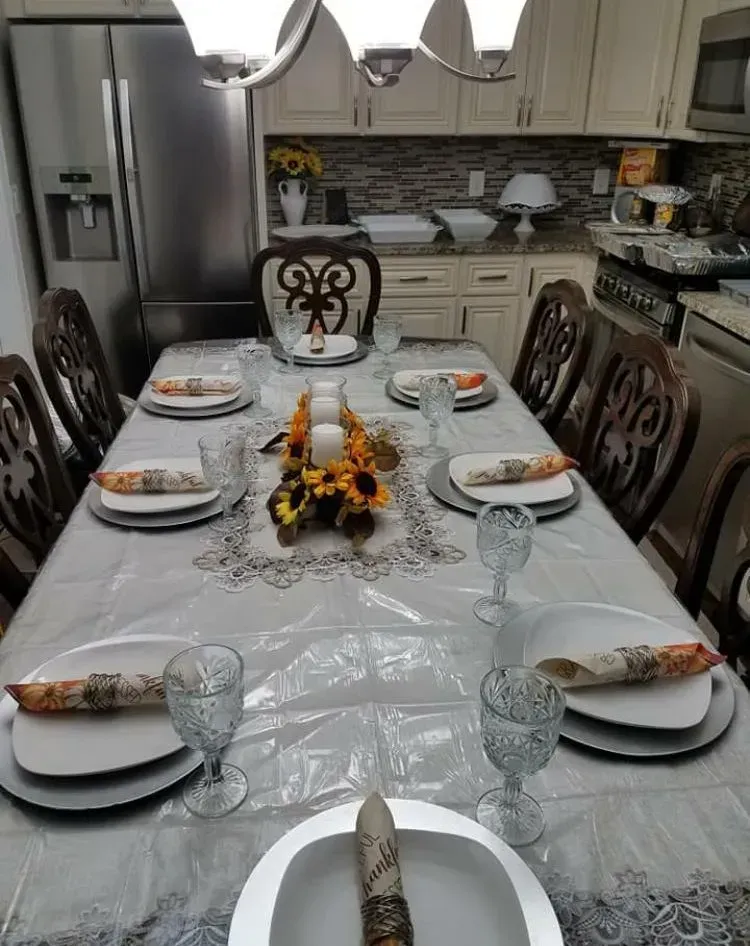 Dining table set for a meal in a kitchen, with place settings, centerpieces, and chairs.