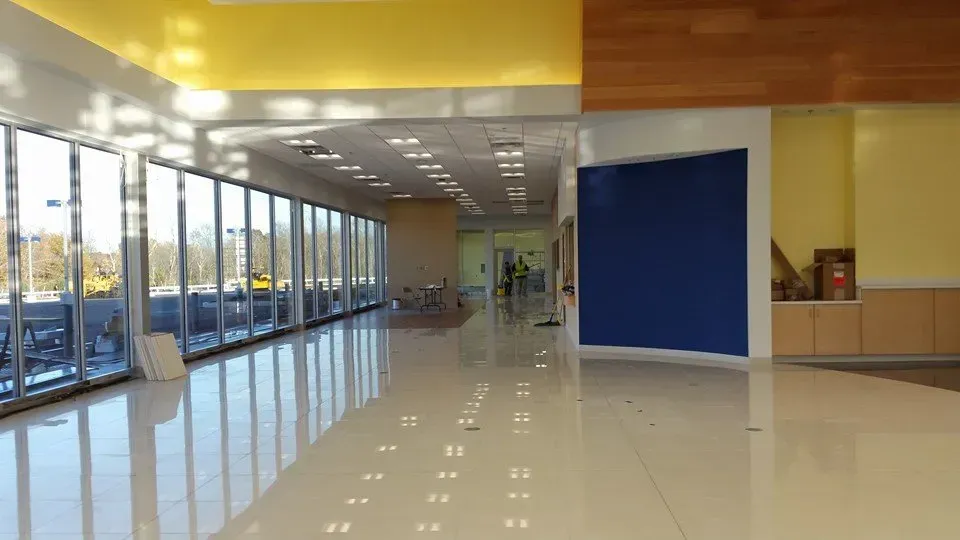 Brightly lit interior with large windows, reflective floors, and yellow and blue walls.