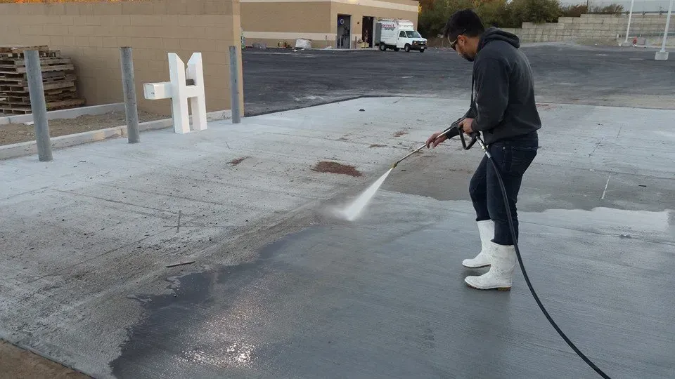 Person power washing a concrete surface with a pressure washer outdoors.
