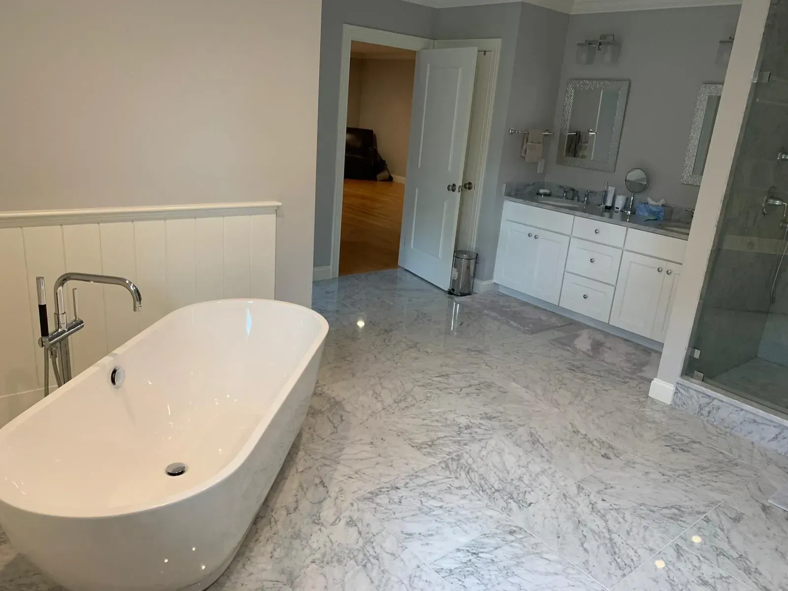 Modern bathroom with a white freestanding tub, marble floor, and double vanity.