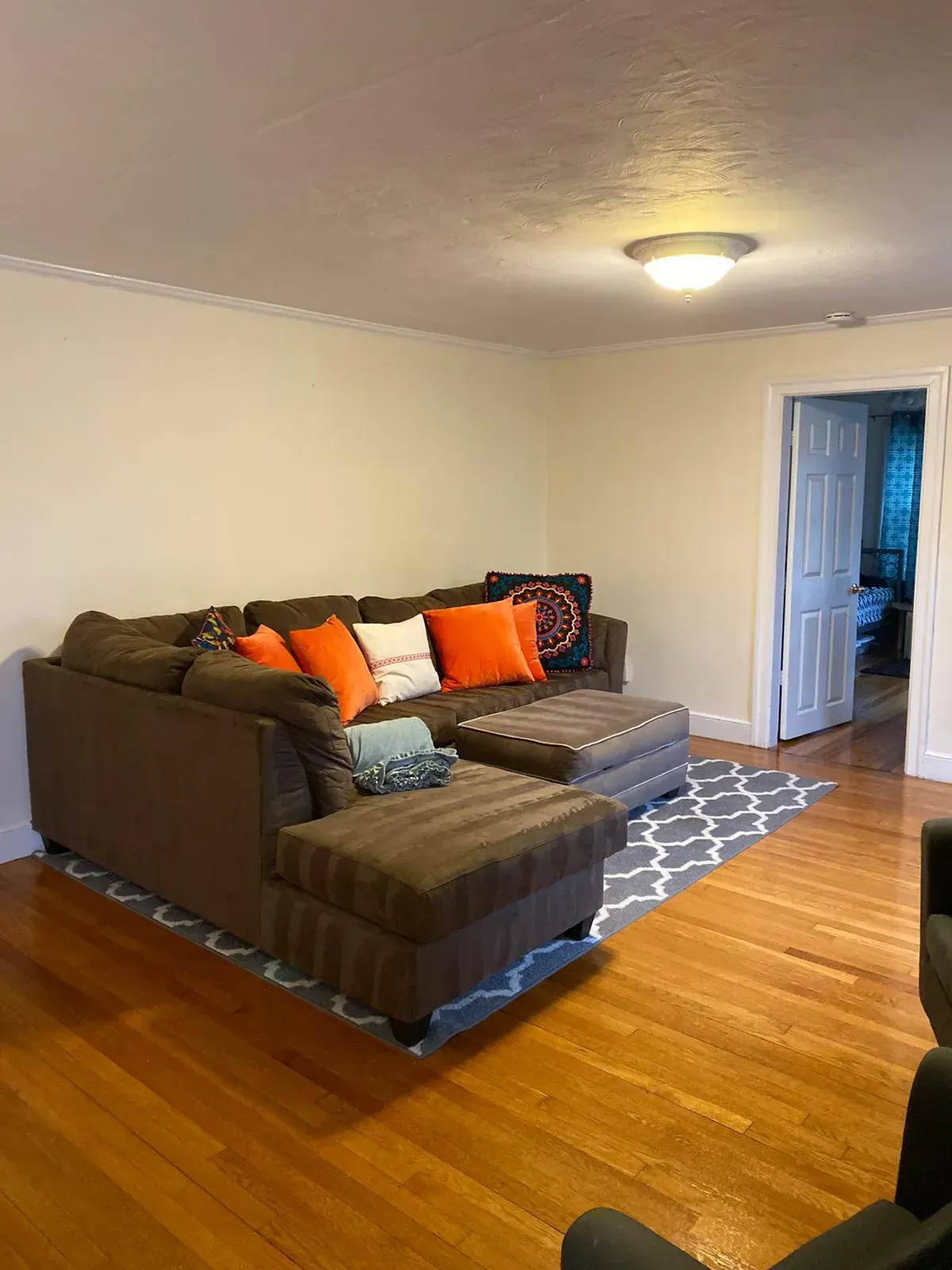 Brown sectional sofa with orange and blue pillows on a gray patterned rug in a room with hardwood floors.