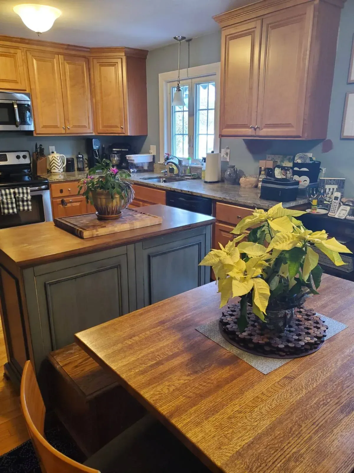 Kitchen with wood cabinets, island, and table. Features plants, appliances, and a window.