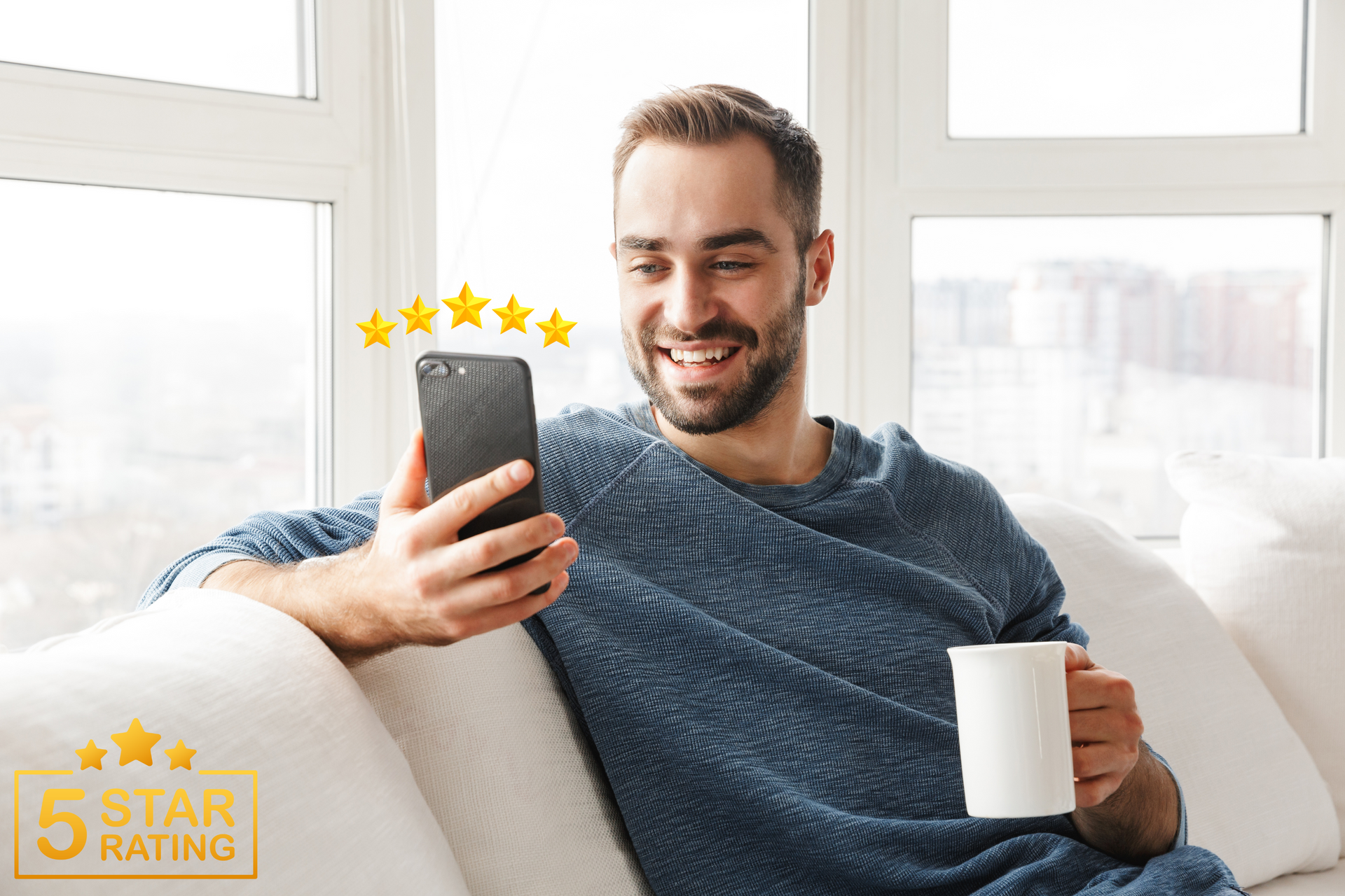 A man is sitting on a couch using a cell phone and holding a cup of coffee.