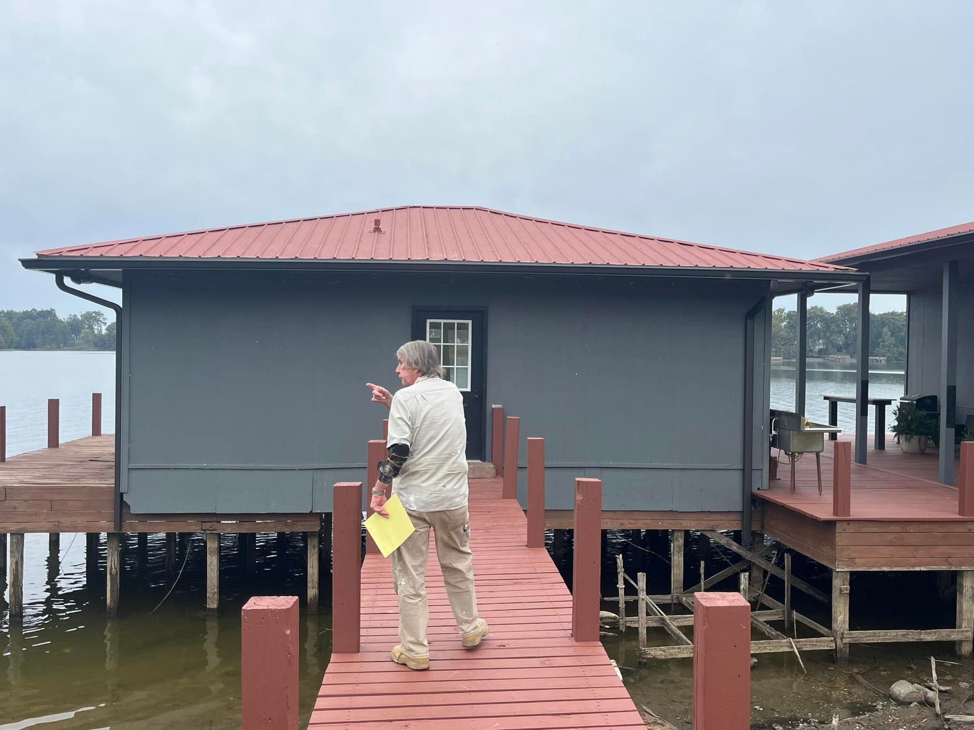 A man is standing on a dock in front of a house.