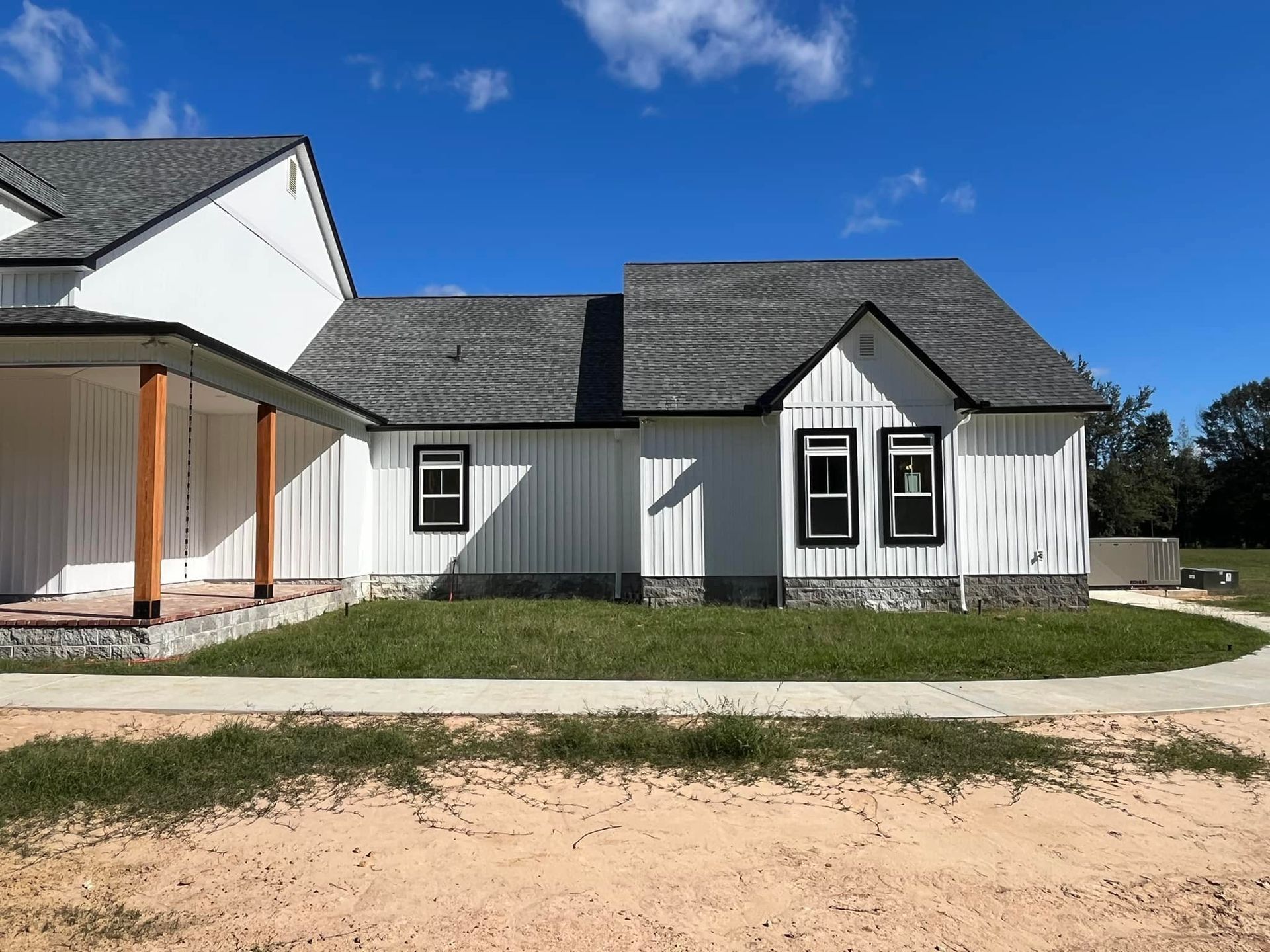A large white house with a gray roof is sitting on top of a dirt field.