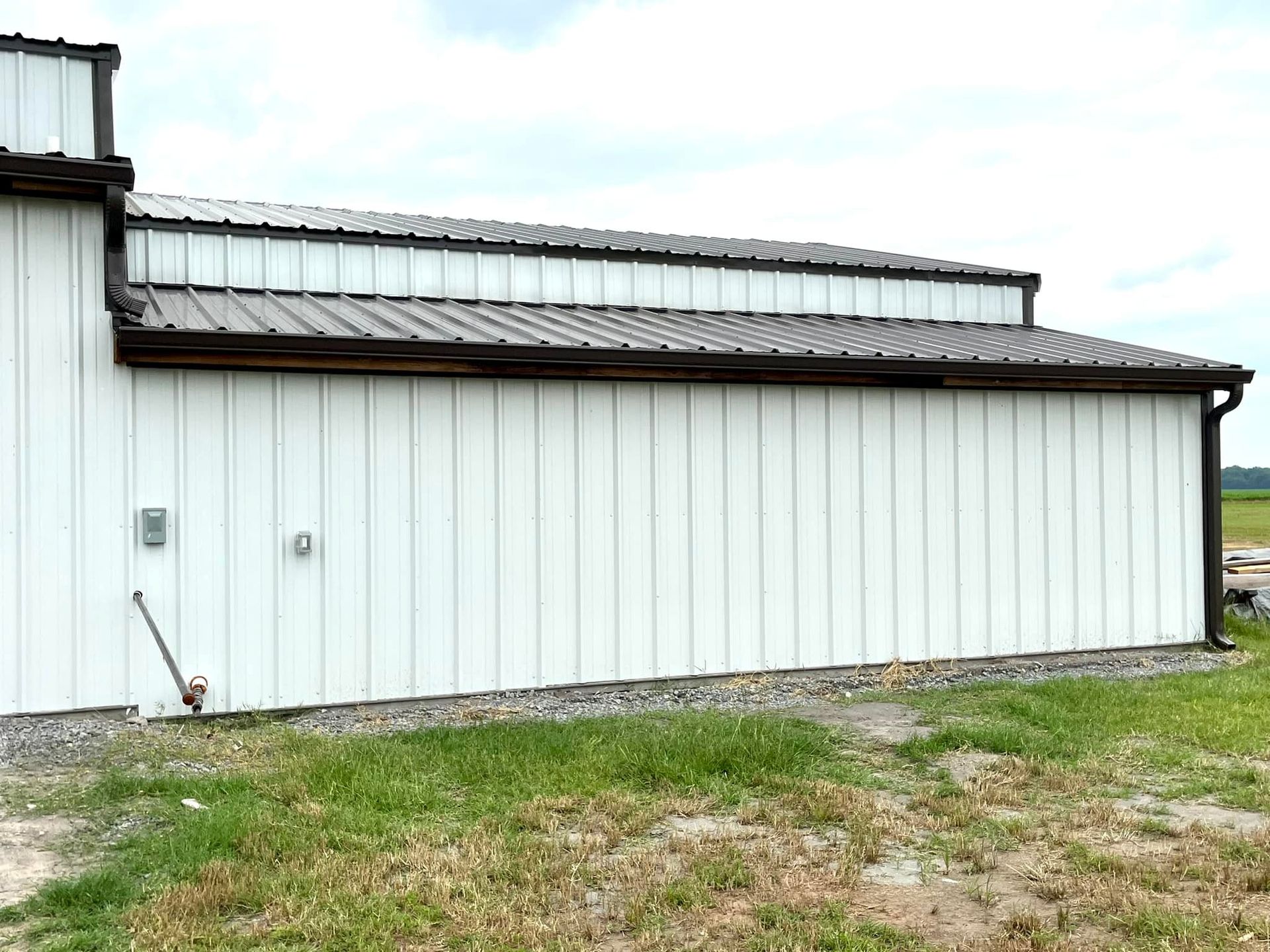 A white building with a brown roof is sitting in the middle of a grassy field.