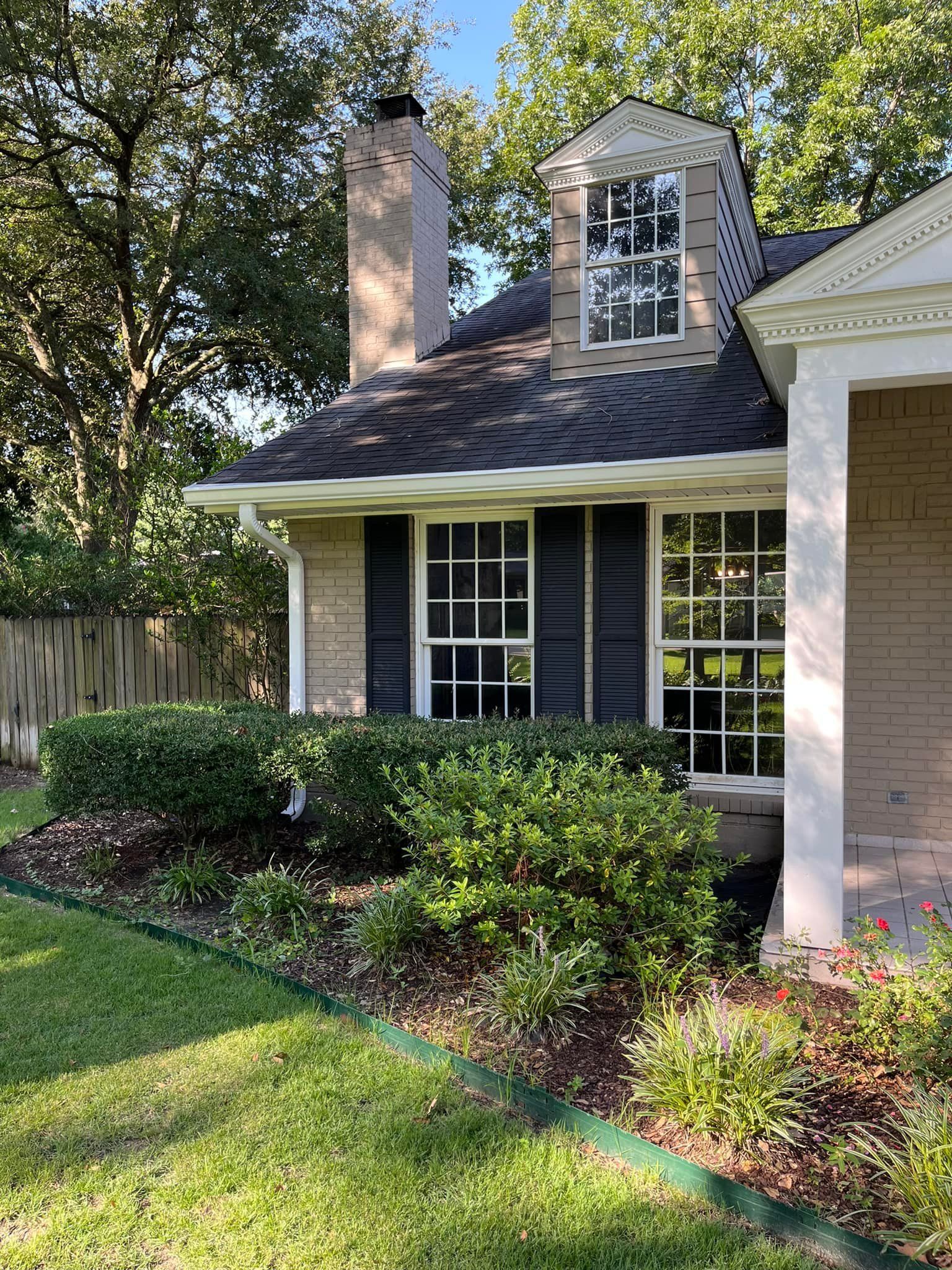 A house with black shutters and white trim is sitting on top of a lush green lawn.