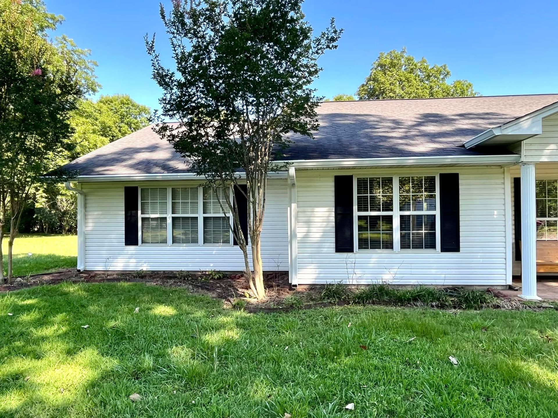 A white house with black shutters and a tree in front of it.