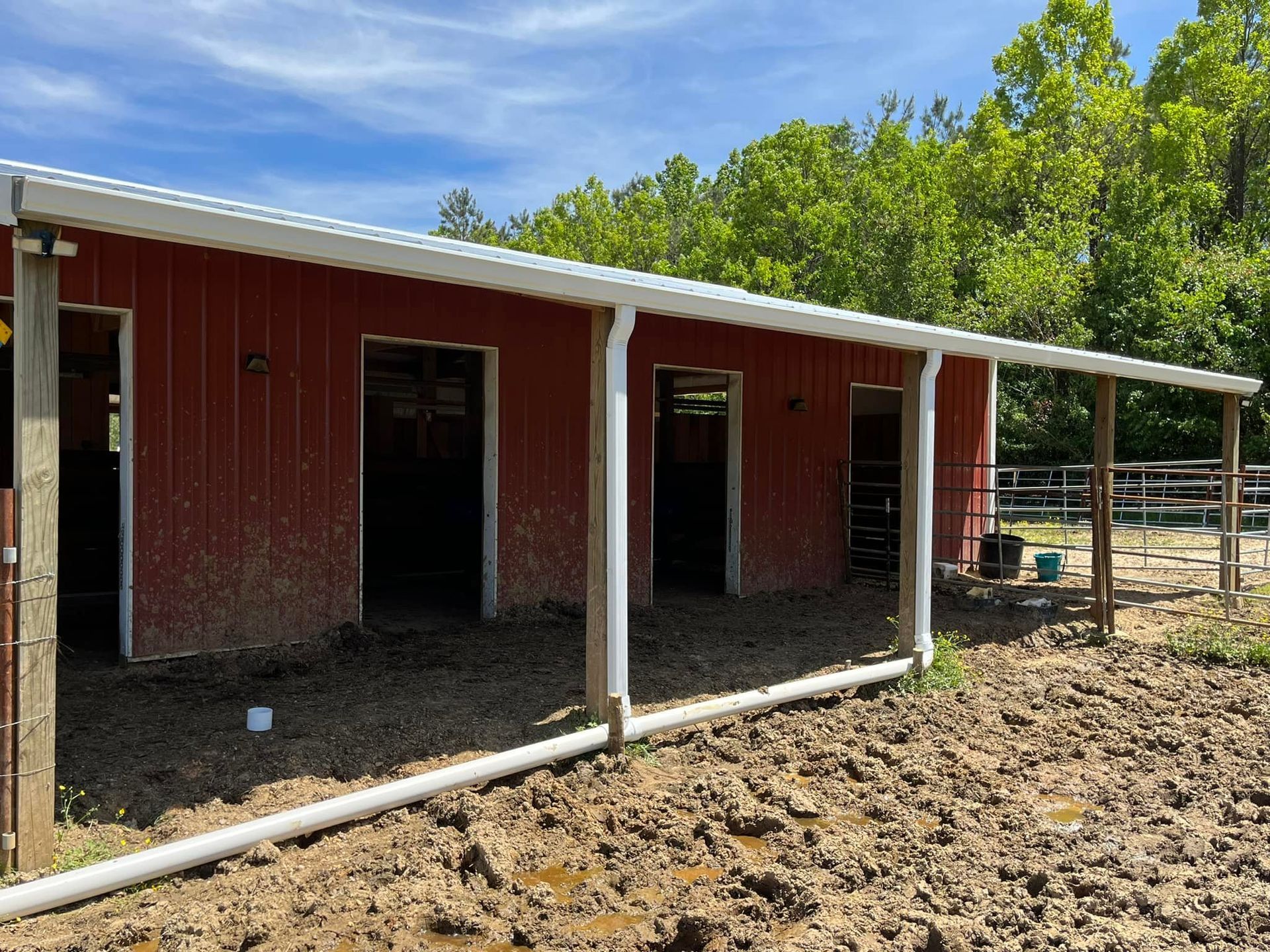 A red barn with a white roof is sitting in the middle of a dirt field.