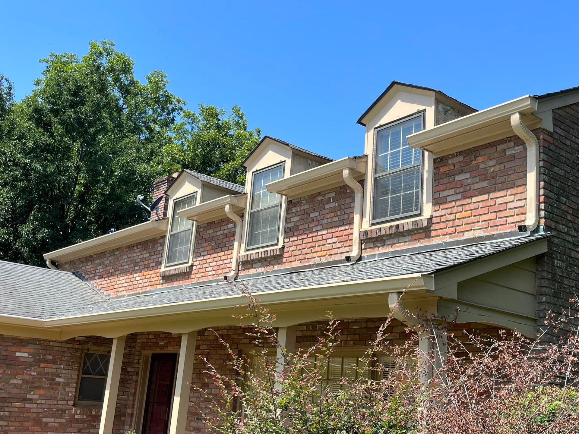 A brick house with a porch and gutters on a sunny day.