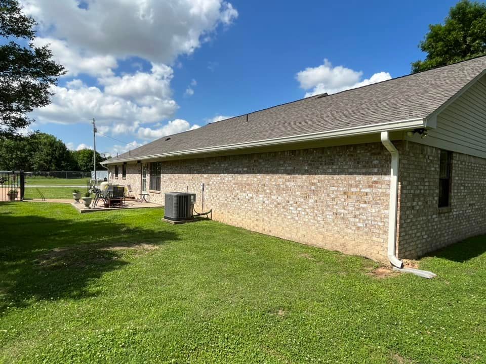 A brick house with a gray roof is sitting in the middle of a lush green field.