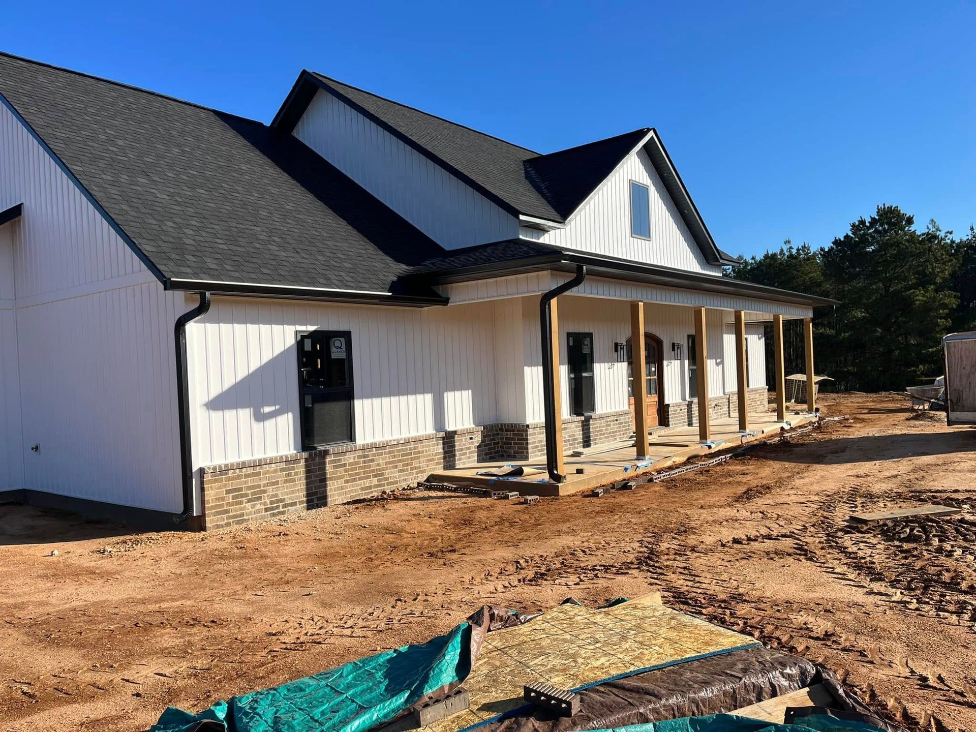 A white house with a black roof is being built in a dirt field.