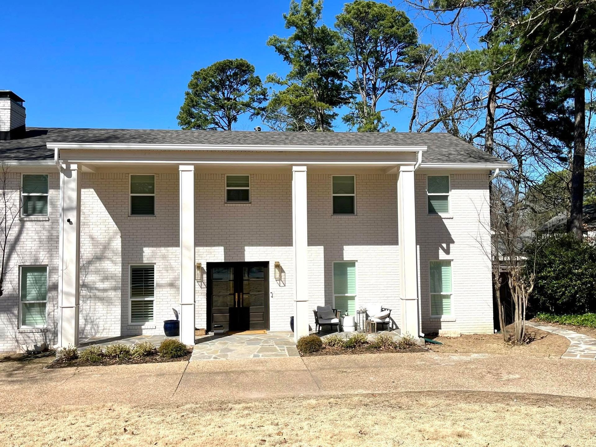 A large white house with a porch and trees in the background