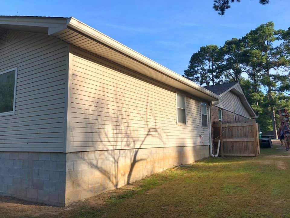 The side of a mobile home with a fence and trees in the background.