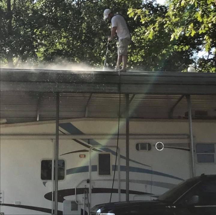 A man is spraying water on the roof of a trailer