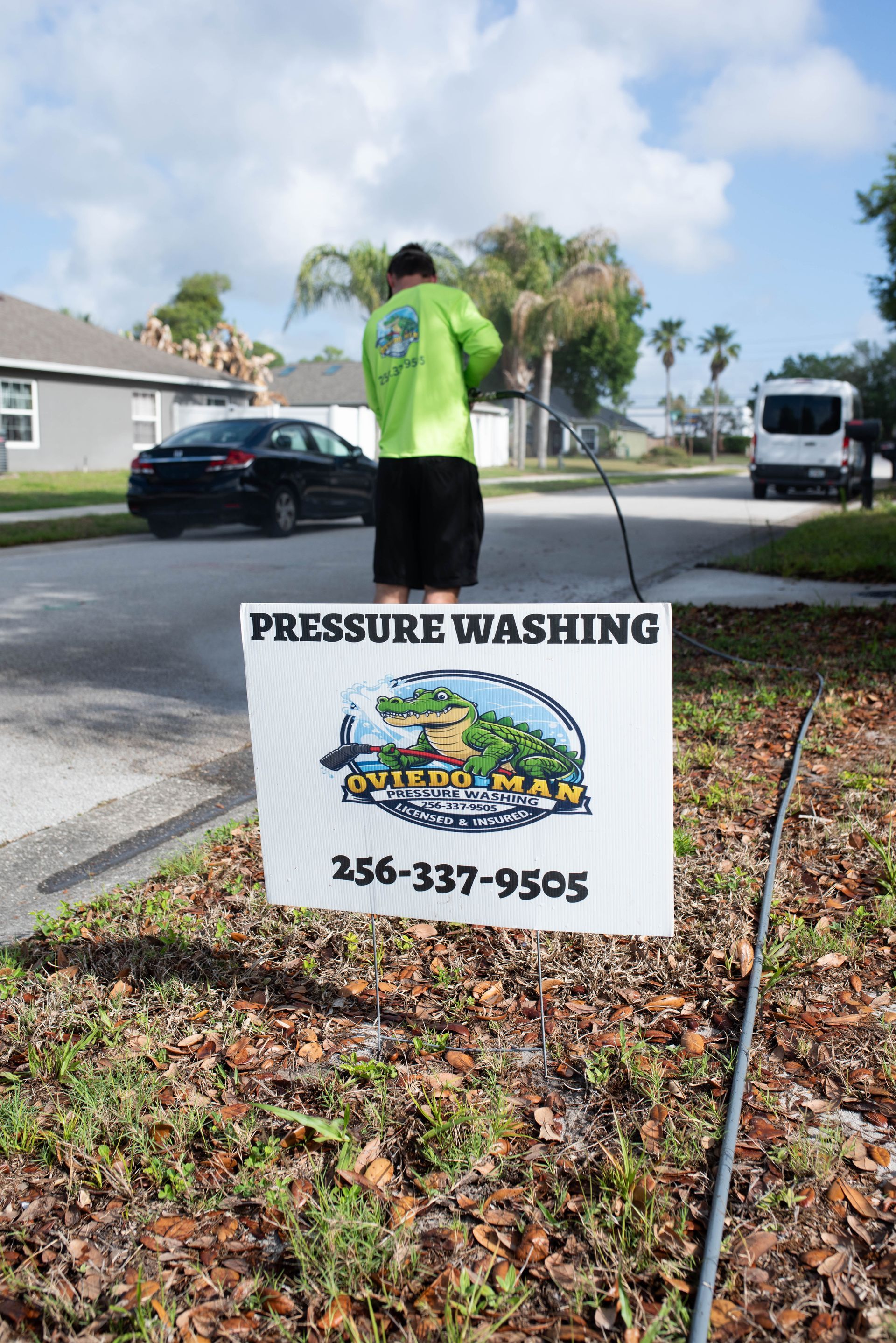 A person in a bright green shirt pressure washes a surface near a 
