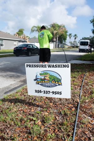 A person in a bright green shirt pressure washes a surface near a