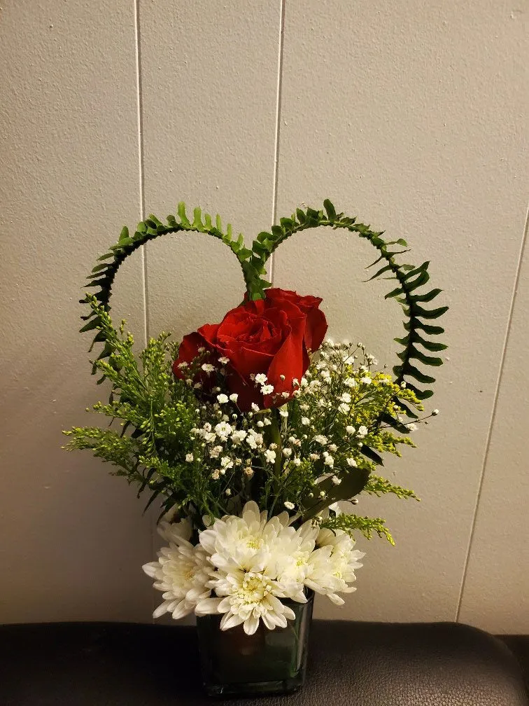 Heart shaped vase filled with flowers and ferns