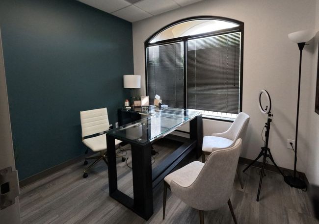 A small office with a desk and chairs in front of a window.